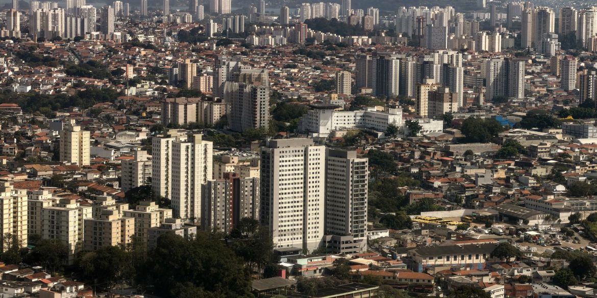 Mãos digitando em notebook com gráficos e mapas do Brasil na tela